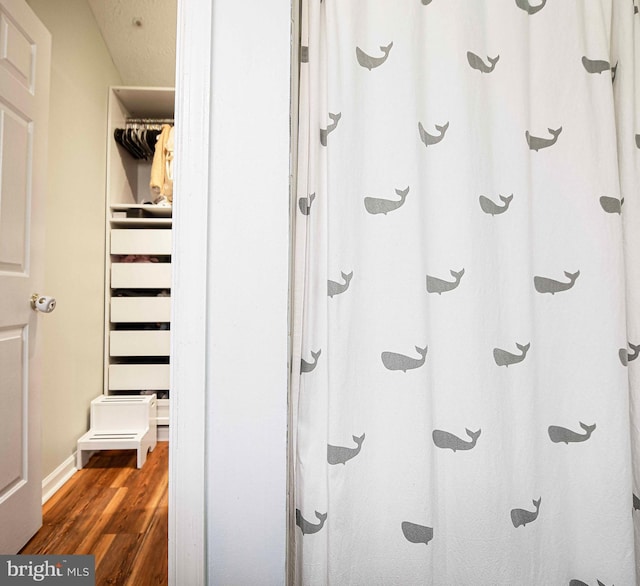bathroom featuring wood finished floors, walk in shower, and baseboards