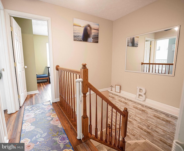 hallway featuring an upstairs landing, wood finished floors, baseboards, and a textured ceiling