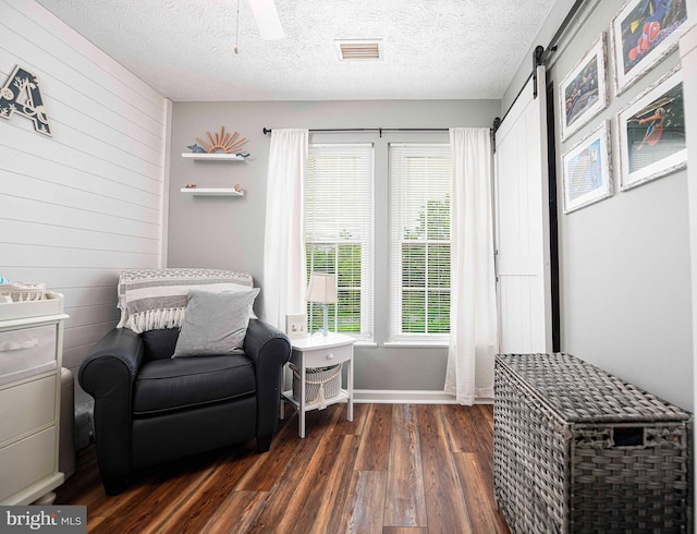 sitting room with dark wood-style floors, wood walls, baseboards, a barn door, and a textured ceiling