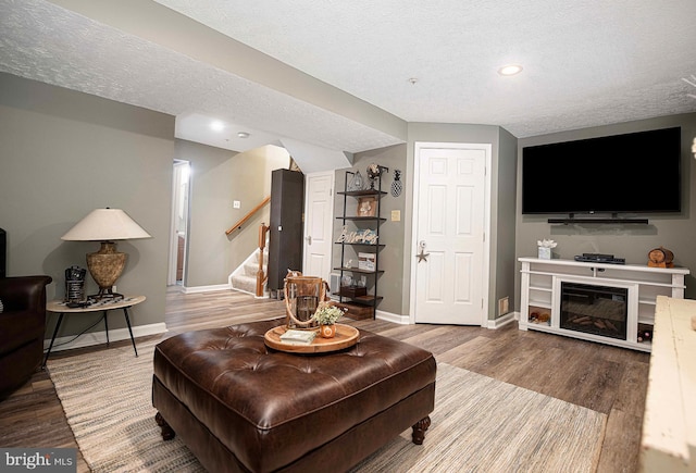 living area with a textured ceiling, stairs, baseboards, wood finished floors, and recessed lighting