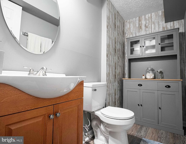bathroom featuring wallpapered walls, wood finished floors, toilet, a textured ceiling, and vanity