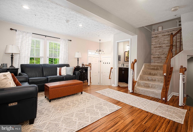 living room with a textured ceiling, stairs, wood finished floors, a chandelier, and baseboards
