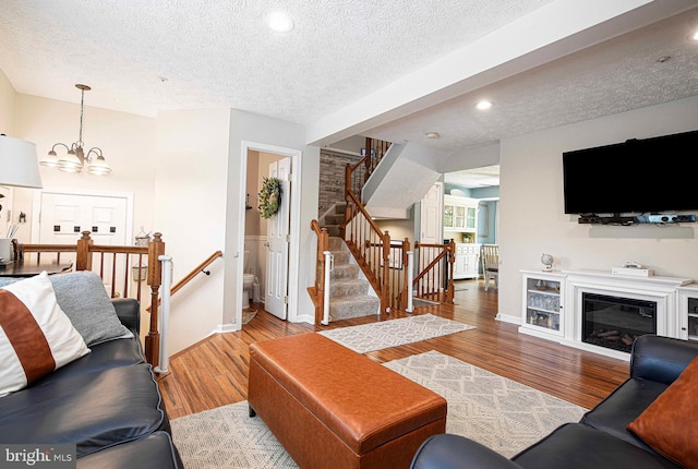 living room with a textured ceiling, wood finished floors, baseboards, a chandelier, and stairway