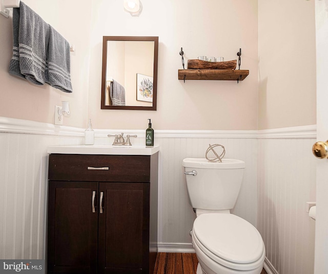 bathroom with a wainscoted wall, toilet, vanity, and wood finished floors