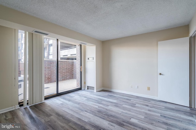 spare room with wood finished floors, a textured ceiling, and baseboards