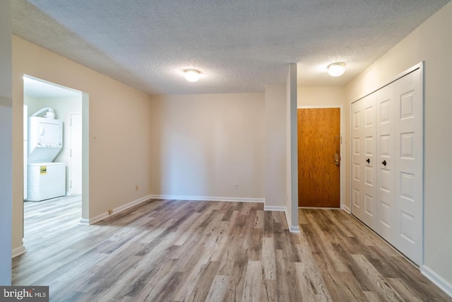 foyer entrance featuring stacked washer / drying machine, wood finished floors, a textured ceiling, and baseboards