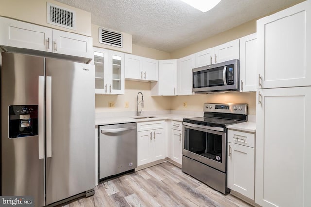 kitchen with stainless steel appliances, a sink, light countertops, light wood-style floors, and a textured ceiling