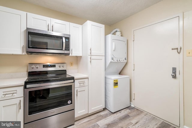 kitchen with stainless steel appliances, stacked washer / drying machine, light wood-style floors, light countertops, and white cabinets