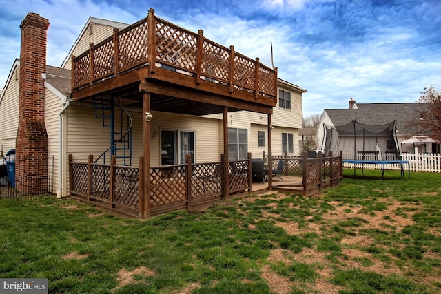back of house featuring a wooden deck, a trampoline, and a chimney