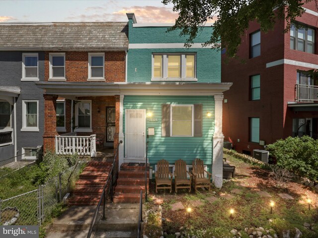view of front of home featuring brick siding, central air condition unit, a porch, and mansard roof