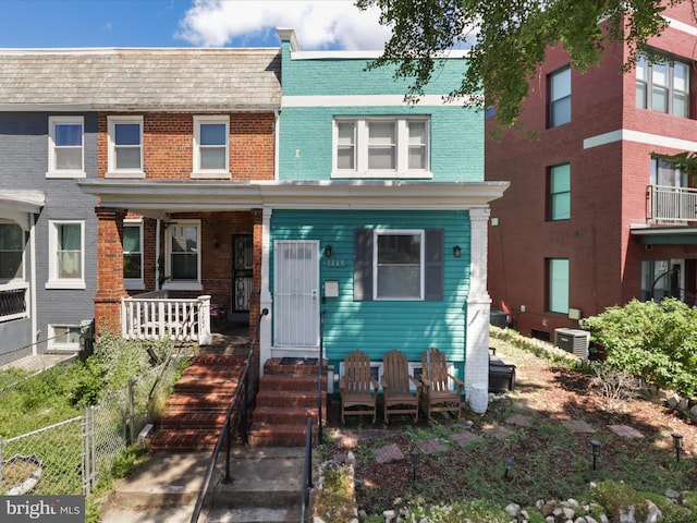 view of property with brick siding, central AC, a porch, and mansard roof