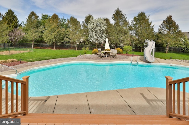 view of swimming pool with a water slide, a patio area, and view of wooded area