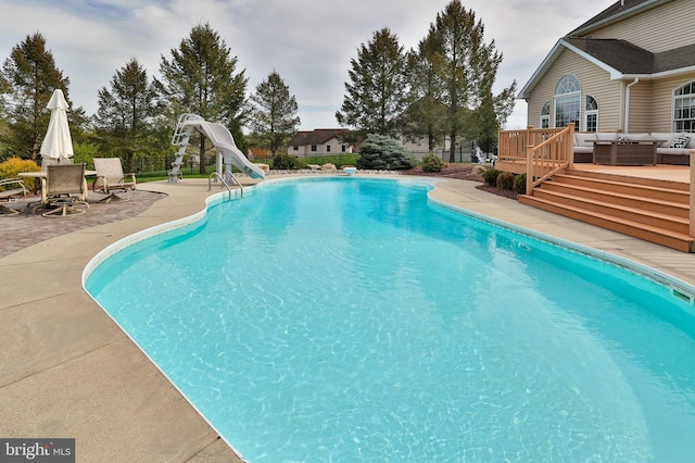 view of pool with a water slide, an outdoor hangout area, a wooden deck, and a patio area