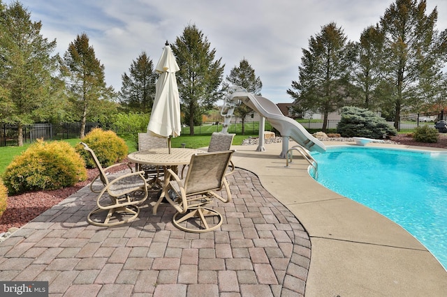 view of pool with a patio, a water slide, fence, and outdoor dining space