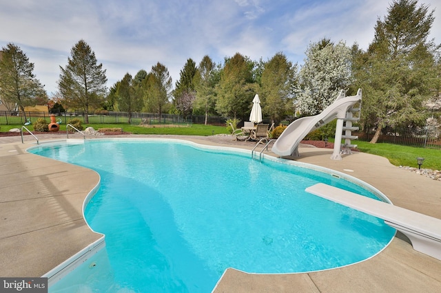 view of pool with a water slide, a diving board, a patio area, and view of scattered trees