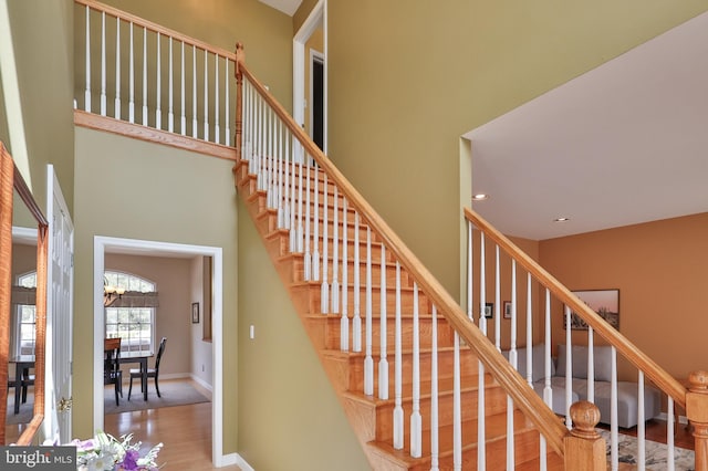 staircase featuring wood finished floors, a towering ceiling, baseboards, a chandelier, and recessed lighting