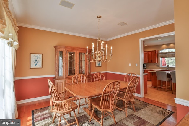 dining space with light wood-style floors, a chandelier, crown molding, and baseboards