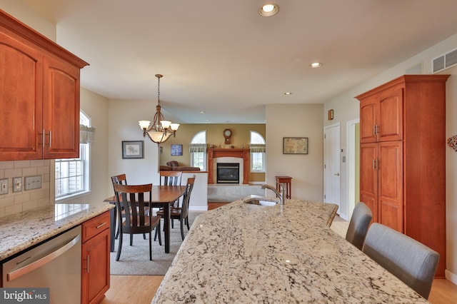 kitchen with stainless steel dishwasher, a glass covered fireplace, light wood-type flooring, light stone countertops, and backsplash