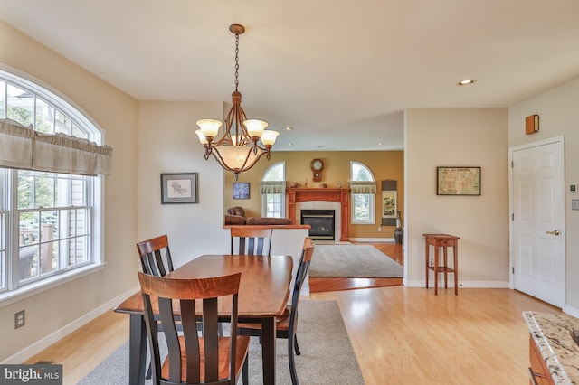 dining room featuring light wood-type flooring, recessed lighting, a chandelier, a fireplace with flush hearth, and baseboards