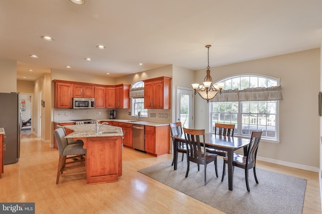 kitchen with stainless steel appliances, a chandelier, a center island with sink, recessed lighting, and light stone countertops