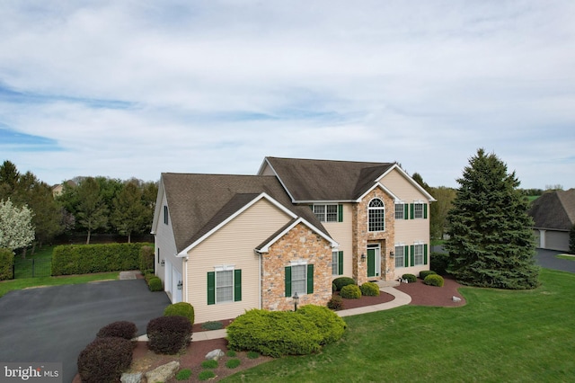 view of front of house featuring stone siding, a front yard, asphalt driveway, and a garage
