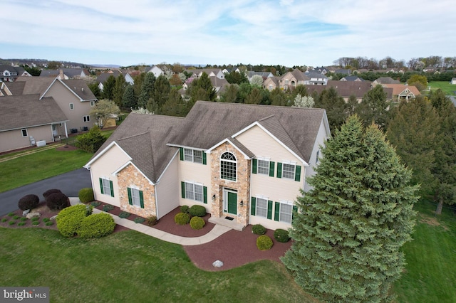 view of front of house with stone siding, a residential view, a front yard, and a shingled roof