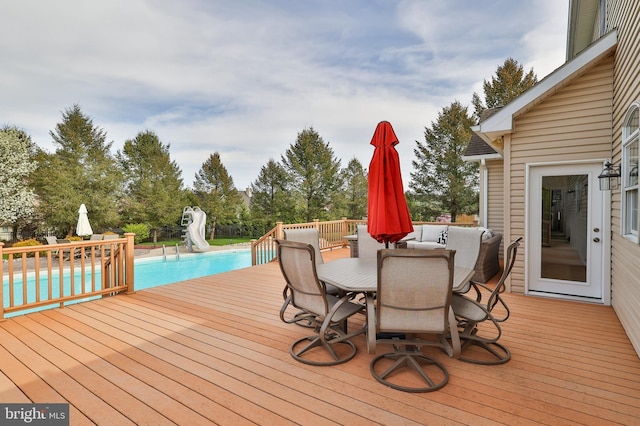 wooden deck with outdoor dining area, an outdoor pool, and view of scattered trees