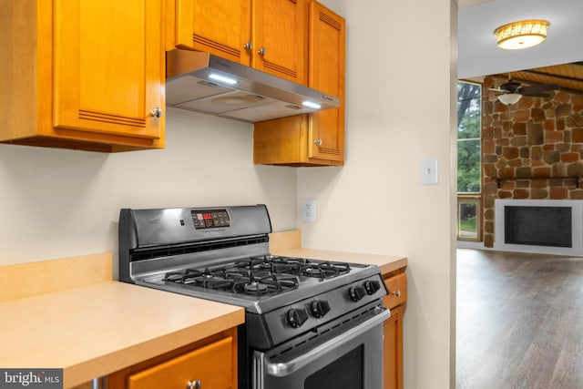 kitchen with stainless steel range with gas stovetop, under cabinet range hood, light countertops, wood finished floors, and brown cabinets