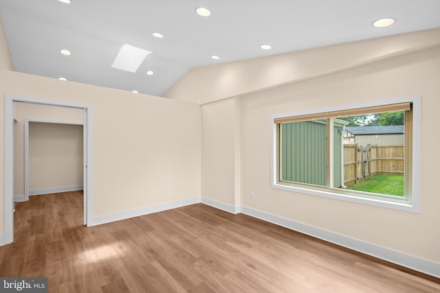 empty room with a skylight, wood finished floors, lofted ceiling, recessed lighting, and baseboards