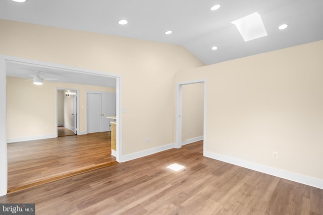 empty room featuring a skylight, light wood-type flooring, vaulted ceiling, baseboards, and recessed lighting