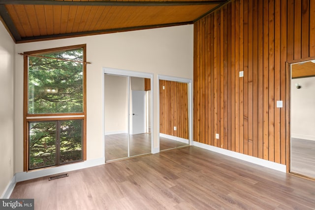 unfurnished bedroom featuring wood ceiling, lofted ceiling, wood finished floors, two closets, and baseboards