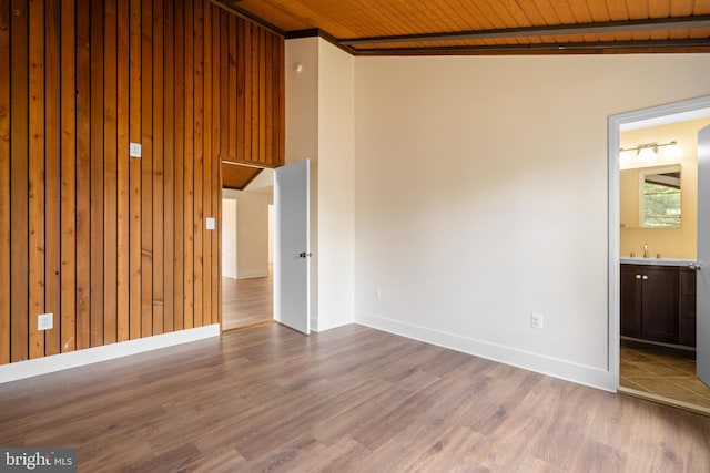 spare room with wood ceiling, wood finished floors, baseboards, a sink, and wooden walls
