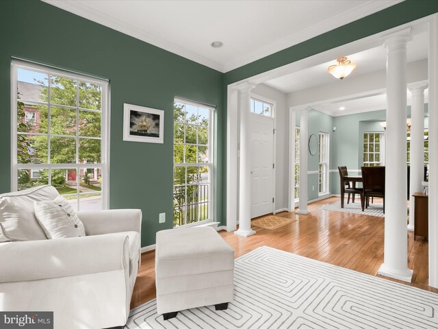 living room with decorative columns, light wood-style floors, crown molding, and baseboards