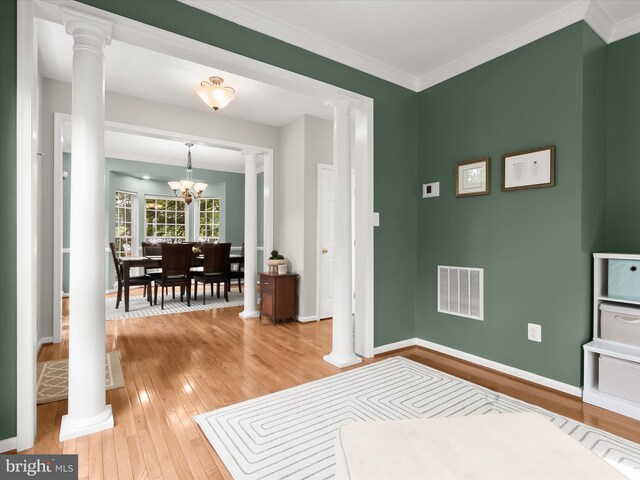 entrance foyer with decorative columns, light wood-style floors, a chandelier, baseboards, and ornamental molding