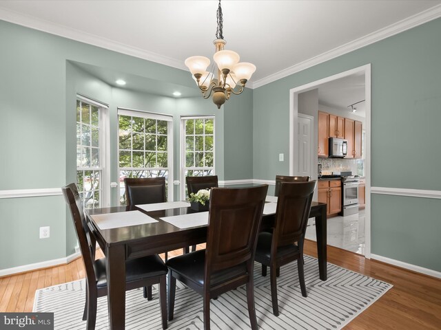dining room featuring a chandelier, ornamental molding, light wood finished floors, and baseboards