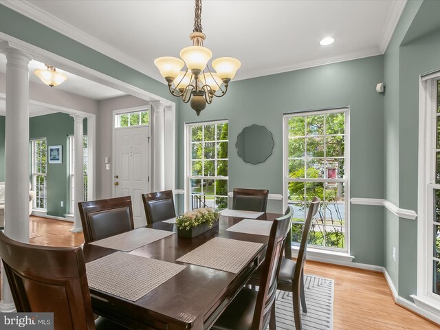 dining space featuring ornate columns, a chandelier, baseboards, light wood-style floors, and ornamental molding