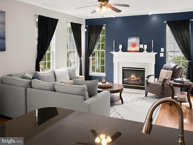 living room with a ceiling fan, wood finished floors, and a glass covered fireplace