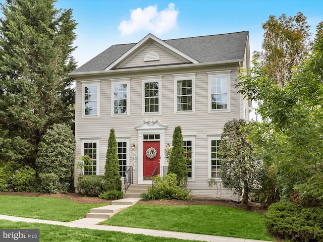 colonial inspired home with a front lawn and roof with shingles