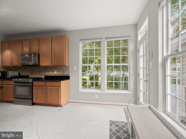 kitchen featuring gas range, stainless steel microwave, light marble finish floors, and tasteful backsplash