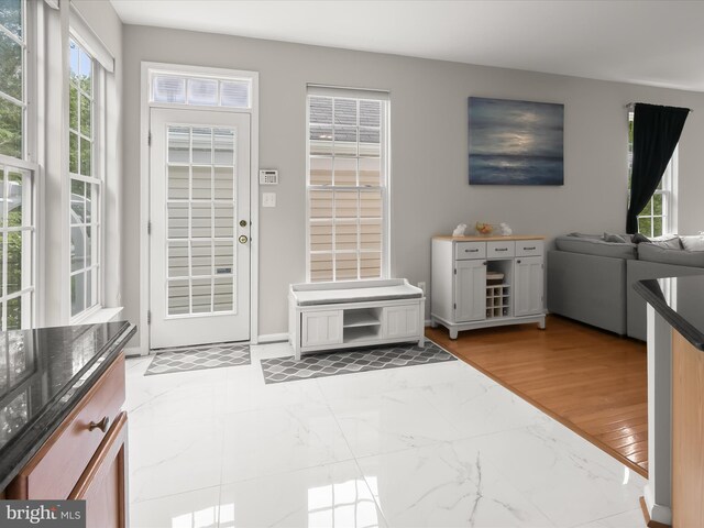doorway featuring plenty of natural light, light marble finish flooring, and baseboards