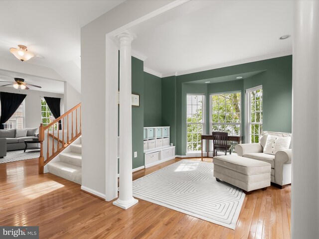 living area featuring decorative columns, hardwood / wood-style floors, ceiling fan, stairway, and crown molding