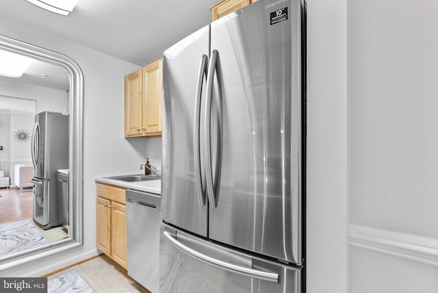 kitchen featuring stainless steel appliances, light brown cabinetry, a sink, light tile patterned floors, and light countertops