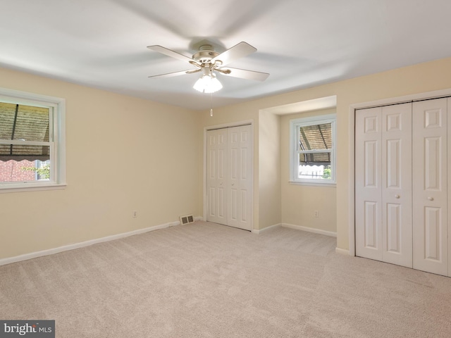 unfurnished bedroom featuring multiple closets, light colored carpet, baseboards, and ceiling fan