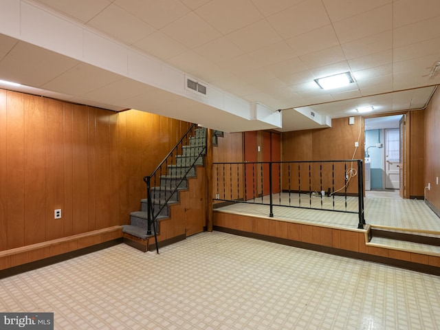 finished basement with baseboards, wooden walls, and stairway