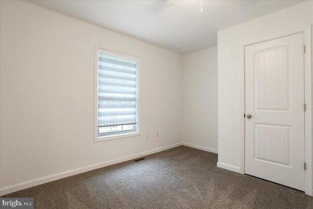 spare room featuring dark carpet and baseboards