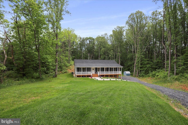 view of front of house with covered porch, a front lawn, a wooded view, and driveway