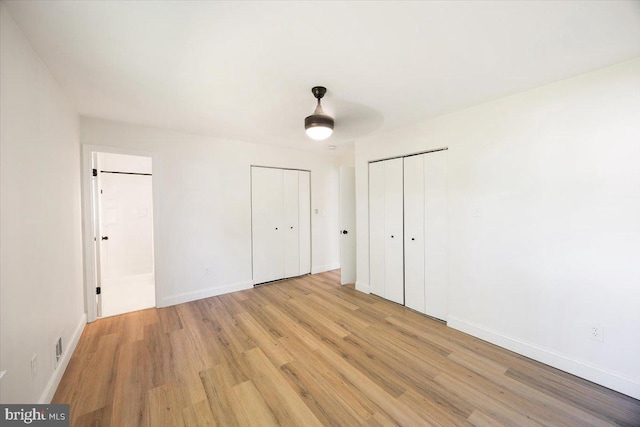unfurnished bedroom featuring light wood-style flooring, baseboards, and multiple closets