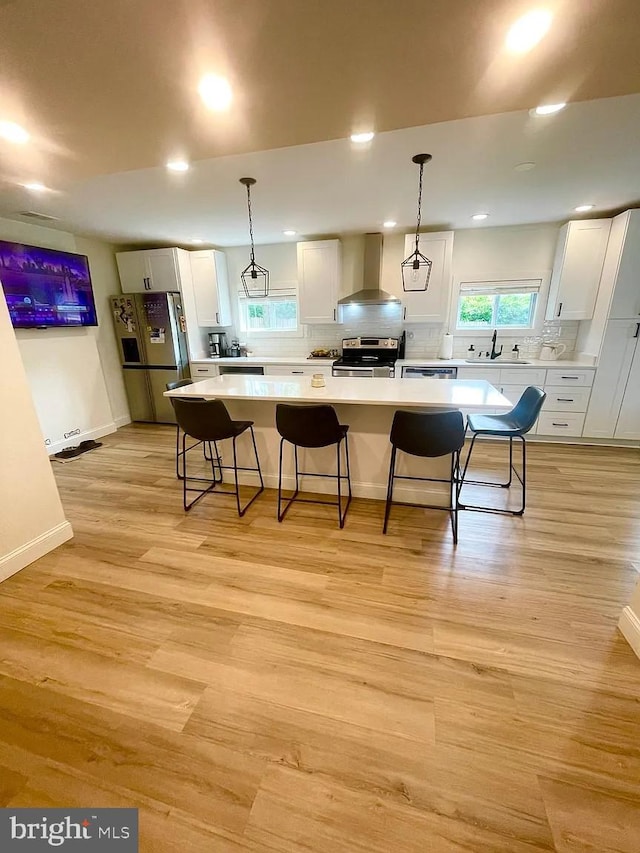 kitchen featuring appliances with stainless steel finishes, a sink, wall chimney exhaust hood, recessed lighting, and a center island