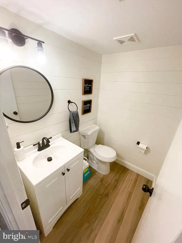 half bath featuring wood finished floors, toilet, and vanity
