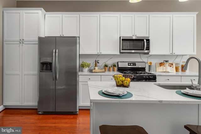 3911 Fleet St, Baltimore, MD 21224 - kitchen featuring appliances with stainless steel finishes, a sink, white cabinets, dark wood-style flooring, and light stone countertops